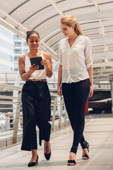 Businesswoman Showing Digital Tablet To Female Colleague On Walkway Bridge In City