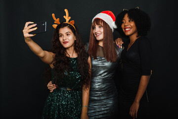 Group of friends at club making selfie and having fun. Cute young women posing with kissing face expression. Relaxed young women making selfie with friend on dark background during christmas celebrati