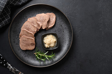 Beef tongue served horseradish sauce and rosemary sprig on black table. Great appetizer for Christmas or banquet. Top view. Space for text.