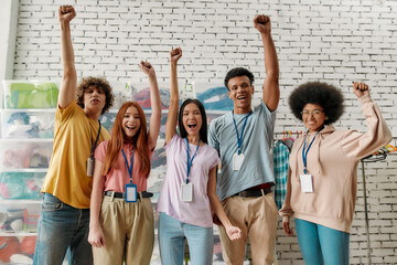 Young diverse volunteer group raised their arms while posing in front of boxes full of clothes, Happy team working for a charity, donating apparel to needy people