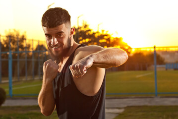 Athlete trains on a sunset background. The boxer warms up near the stadium. Contrasting dramatic shadows on the face as an artistic effect. The face is blurred, the sharpness on the fist.