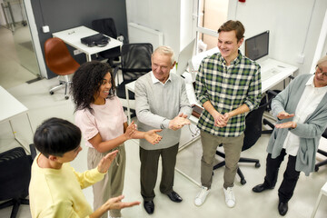 Group of diverse employees applauding while standing together in the office, Aged woman and man,...