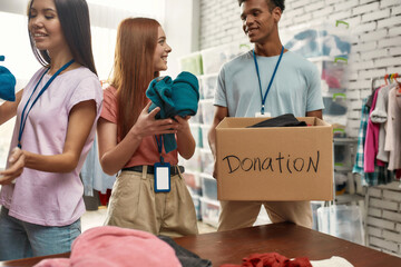 Happy young volunteers sorting, packing clothes in cardboard boxes, Diverse team working together...