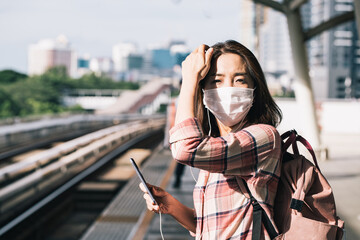 Asian woman wearing surgical face mask against novel coronavirus or corona virus disease (Covid-19) at public train station. Relax and listening music on the way.