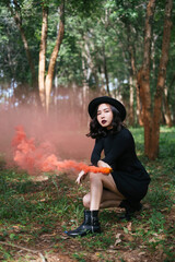 Portrait of asian black witch with red smoke torch in deep forest.
