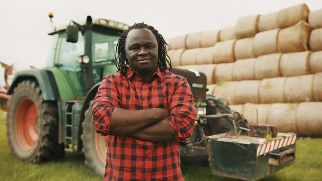 Young african man nodding head as approval with crossed hands over the chest in front of tractor and haystack. Thumbs up. High quality 4k footage
