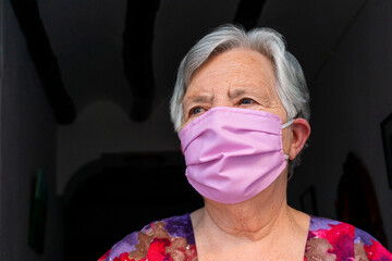 Close-up portrait of a elderly woman with a face mask looking to the side on dark background