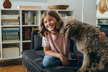 young girl sitting on sofa cuddling with her dog at home