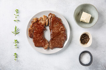 Denver steak. Two prepeared beef steaks on gray plate on concrete background. Top view.
