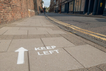 A painted instruction on a city pavement says 'keep left' with a white arrow beside it. Public Safety Sign.UK 