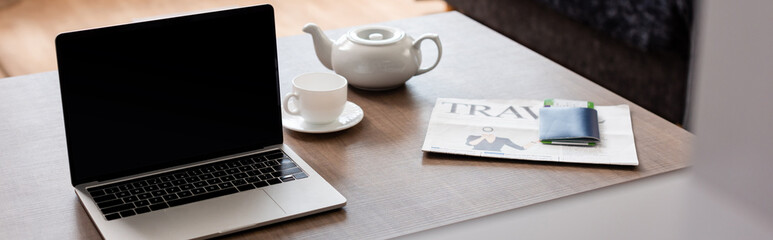 panoramic crop of laptop with blank screen near teapot, cup, travel newspaper and passport with air ticket on table
