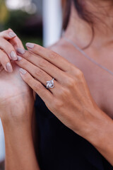 Close up of elegant diamond ring on woman finger. Woman wearing black dress. Love and wedding concept. Soft natural day light and selective focus.   