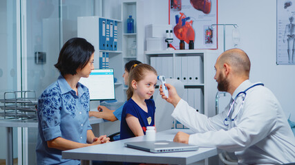 Pediatrician checking temperature and nurse writing on computer. Doctor specialist in medicine providing health care services consultation diagnostic examination treatment in hospital cabinet