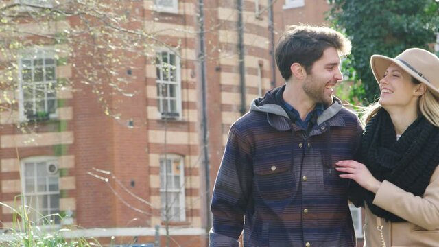 Smiling couple on date walk arm in arm through city park in fall together - shot in slow motion
