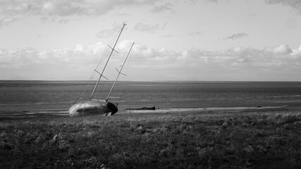 An abandoned old fishing vessel on the beach at Lytham in the UK in a wide black and white image