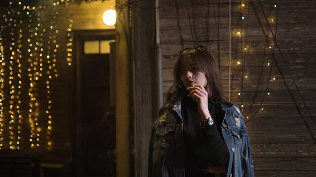 Christmas mood: Young woman smokes cigarette at night with X-mas garland in background