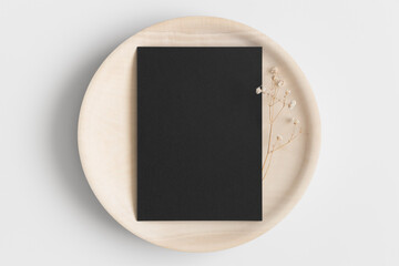 Black invitation card mockup on a wooden plate with a gypsophila. 5x7 ratio, similar to A6, A5.