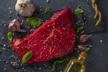 Raw meat beef steak on black background, with herbs and spices, top view.
