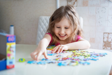 little girl with light wavy hair collects a puzzle at home and has fun.