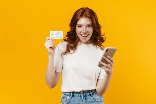 Image of ginger happy girl holding credit card and using cellphone