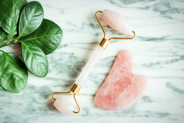 The gua sha and the face roller on marble background, top view.