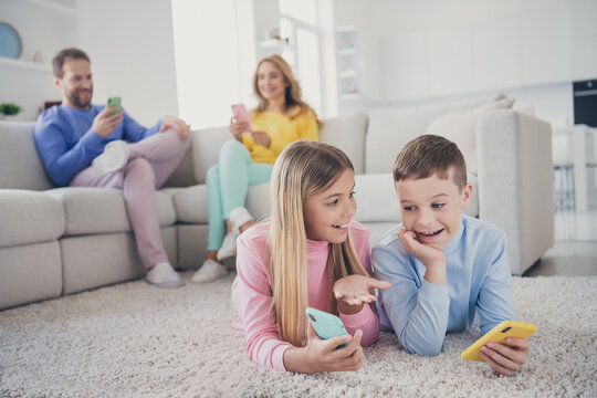 Photo of family people mom dad sit sofa two friends kids lying floor girl show cellphone screen in house indoors