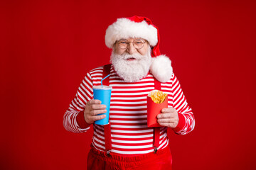 Portrait of his he nice handsome cheerful cheery hungry bearded Santa eating fried potato meal snack drinking tasty lemonade isolated bright vivid shine vibrant red color background
