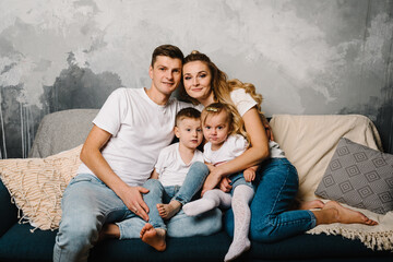 Family portrait of parents and children in denim casual style clothes. Fashion models looking at camera on gray background. Smiling young mother and father with daughter and son posing together.