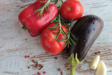 Tomatoes, eggplant, peppers and spices lie on a wooden surface.