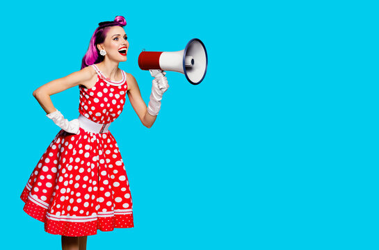 Violet red haired woman using mega phone, shouting something. Girl in pinup style dress in polka dot isolated over aqua blue color background. Retro fashion vintage studio concept. Copy space for text