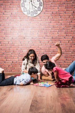 Indian Happy Family Playing Board Games Like Chess, Ludo Or Snack And Ladder At Home In Quarantine