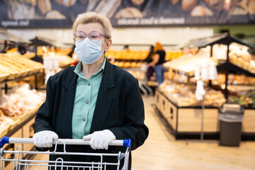 older woman with glasses chooses buns and bread in supermarket bakery