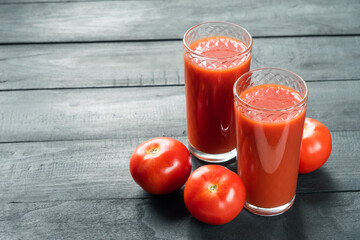 Two glasses of fresh tomato juice and red ripe tomatoes on black wooden background. Selective focus, copyspace