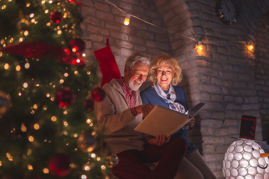 Senior Couple Looking Through Old Photo Album On Christmas Eve