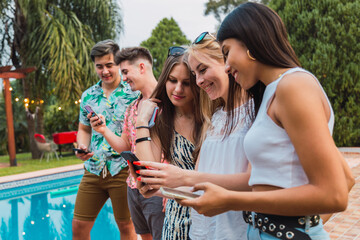 Happy friends with their smartphone in the pool.  Young trendy people enjoy summer. Travel, friendship, youth and tropical concept. Focus on caucasian woman.