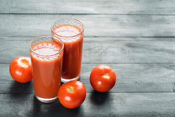 Two glasses of fresh tomato juice and red ripe tomatoes on black wooden background. Selective focus, copyspace