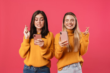 Image of pleased women using smartphones and holding fingers together