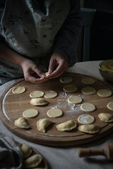Step by step process of making Ukrainian pyrogy (Polish pierogi) with cottage cheese. Woman making pyrogy sitting by the table.