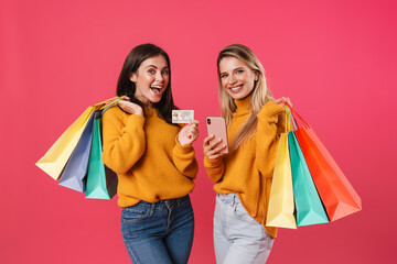 Image of women holding card and cellphone while posing with shopping bags