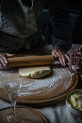 Step by step process of making Ukrainian pyrogy (Polish pierogi) with cottage cheese. Woman rolling a dough on round wooden board.