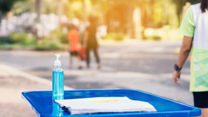 Blue alcohol gel bottle and a register book on the table for athletes to prevent Corona Virus (COVID -19) infection and spread before exercising in public park. New normal lifestyle. Selective focus