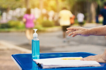 Blue alcohol gel bottle and a register book on the table for athletes to prevent Corona Virus (COVID -19) infection and spread before exercising in public park. New normal lifestyle. Selective focus