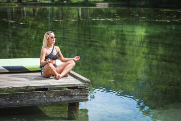 Young Caucasian woman doing seated yoga poses on the dock