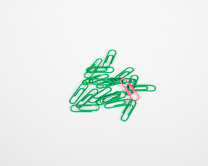 Single pink paper clip on pile of green ones, standing out, excelling, ahead of the pack