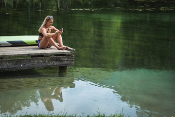 Young Caucasian woman sitting on the dock, looking in a smartphone