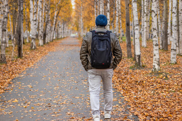A man with a backpack walks along the alley of the autumn park.
