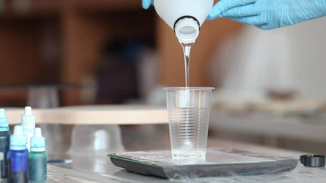 hands pour epoxy into a glass