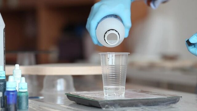 hands pour epoxy into a glass
