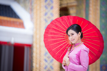 Beautiful woman in a pink Thai dress or a traditional Thai dress is spreading a red umbrella in a Thai temple.