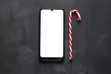 A smartphone with a white screen lies on a dark background next to a red candy cane.